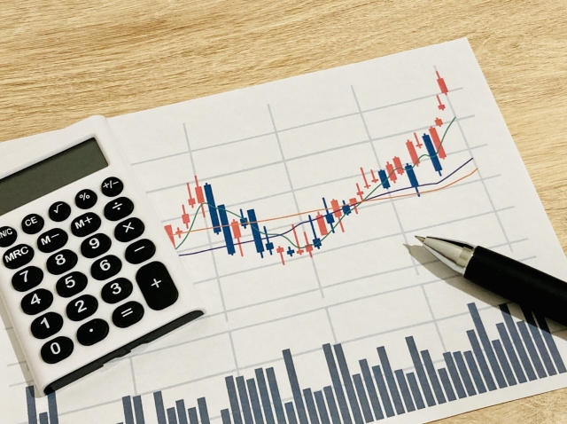 電卓とペンの横に、右肩上がりの推移が描かれたグラフ資料のイメージ