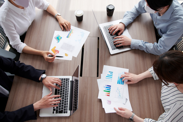 資料を囲みながらノートPCで打ち合わせをしている会議風景